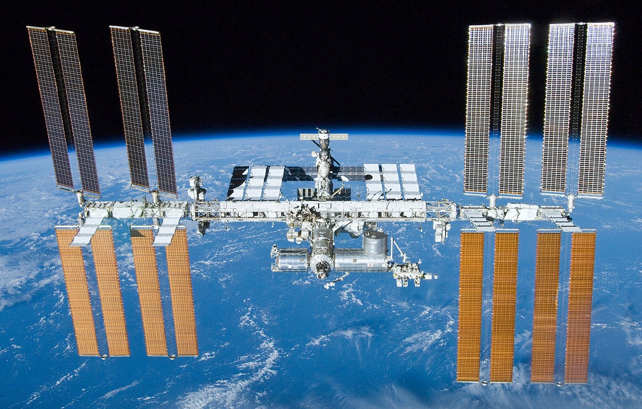 the International Space Station in sunlight with the curved blue surface of the Earth behind it